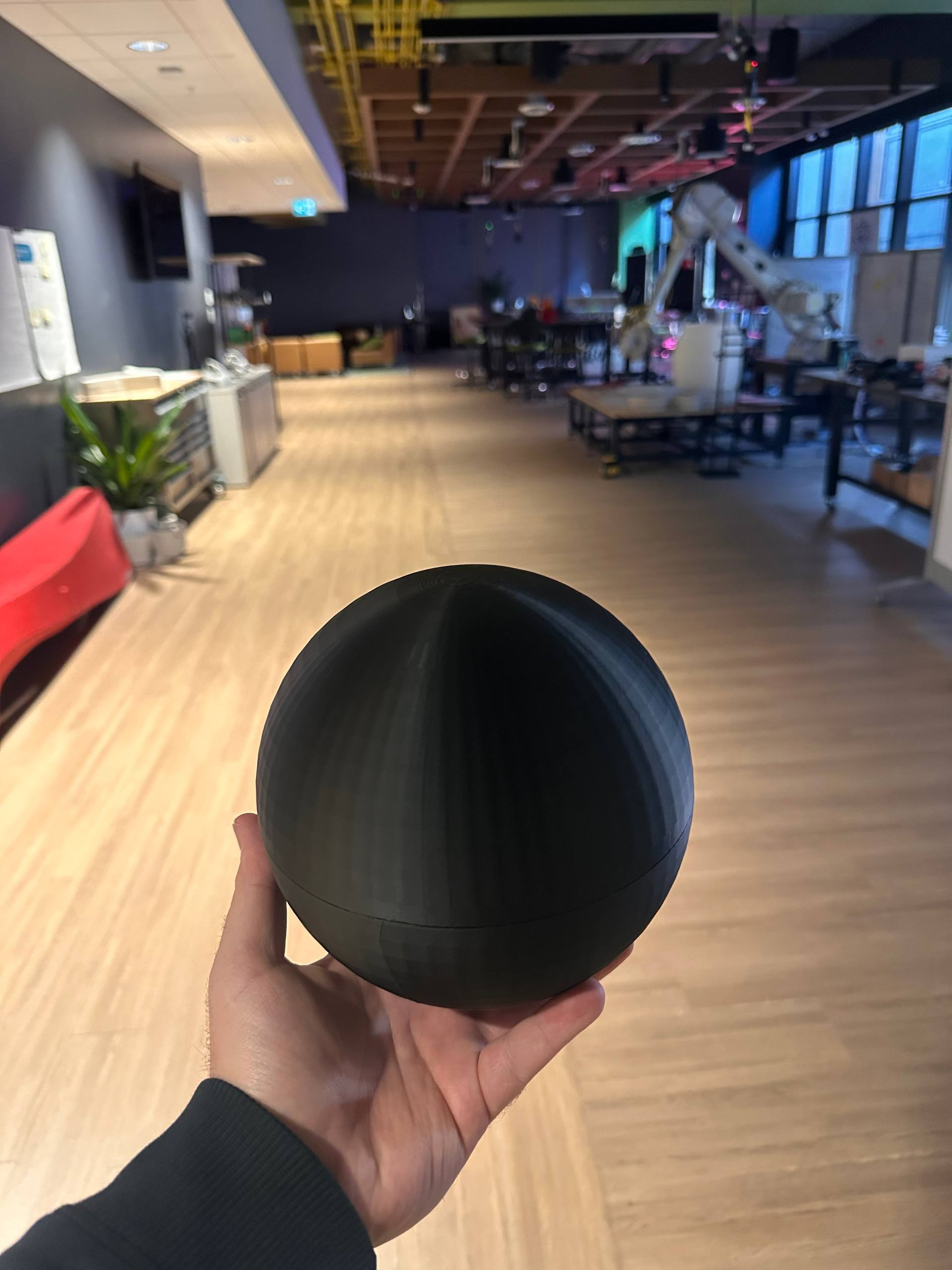 Black prototype sphere held in one hand in a workshop